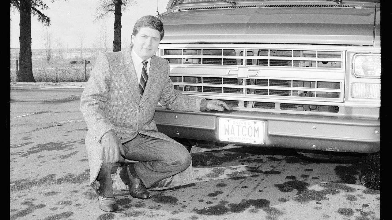 Ian McPhee kneeling beside a car with a license plate that reads 